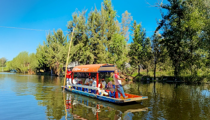 Trajinera boat with people enjoying a festive ride on Xochimilco River, Mexico City.