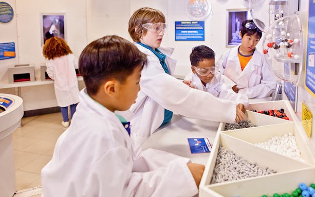 Children in lab coats exploring a science exhibit at a Houston museum.