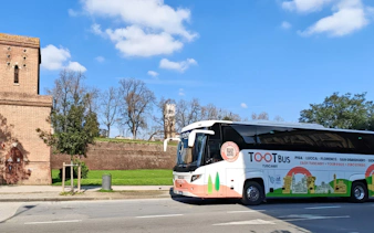 Tootbus tour bus in Tuscany near historic brick building and green landscape.