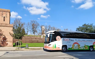 Tootbus tour bus in Tuscany near historic brick building and green landscape.