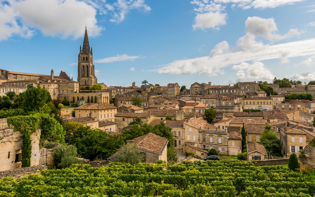 Saint Emilion village with vineyards and church tower under blue sky.