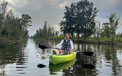 Kayaker paddling through Xochimilco canals with lush greenery in the background.