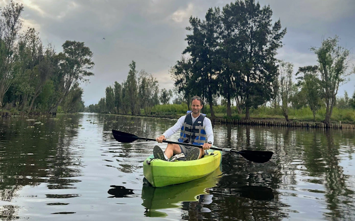 Kayaker paddling through Xochimilco canals with lush greenery in the background.