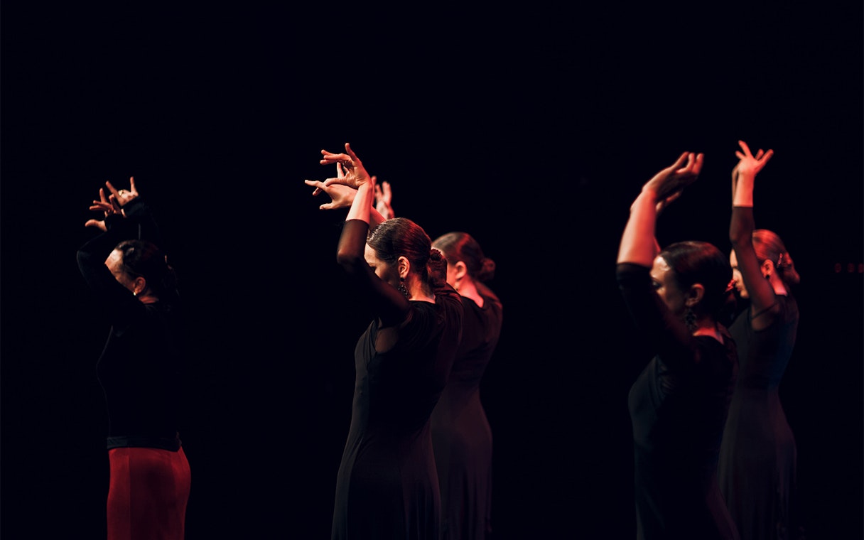 Flamenco dancers performing on stage with raised arms.