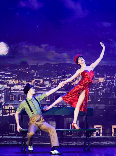 Dancers performing in front of Paris skyline with Eiffel Tower during New Year's Eve cabaret show.