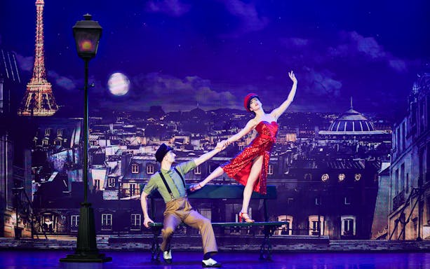 Dancers performing in front of Paris skyline with Eiffel Tower during New Year's Eve cabaret show.