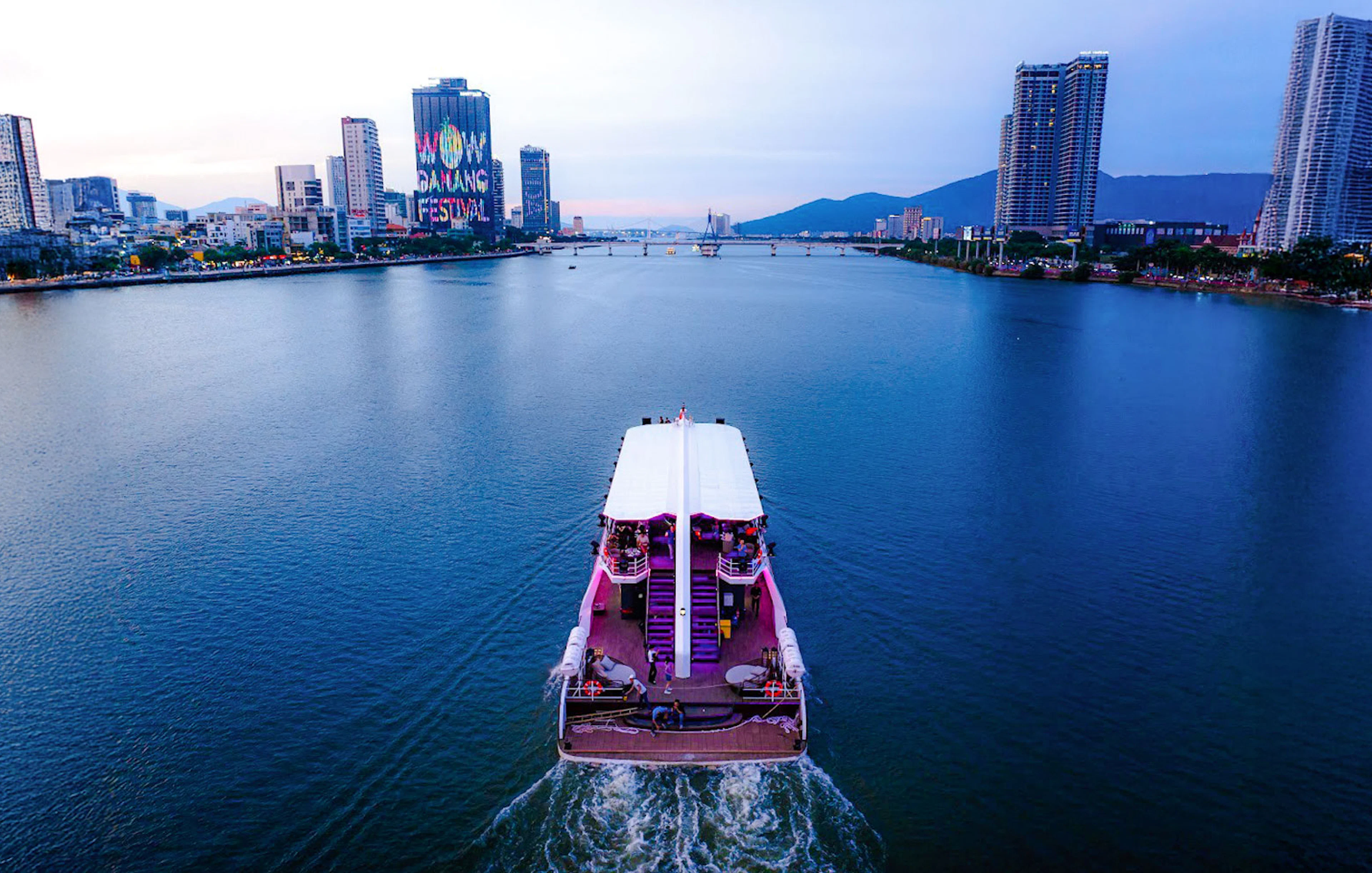 Cruise ship on Han River with Da Nang skyline and festival sign in view.