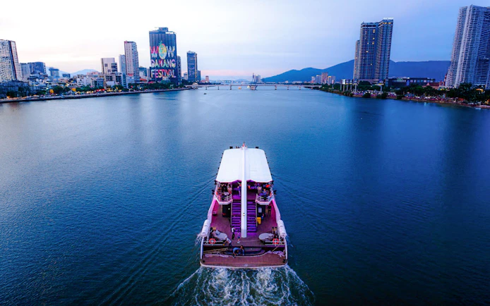 Cruise ship on Han River with Da Nang skyline and festival sign in view.