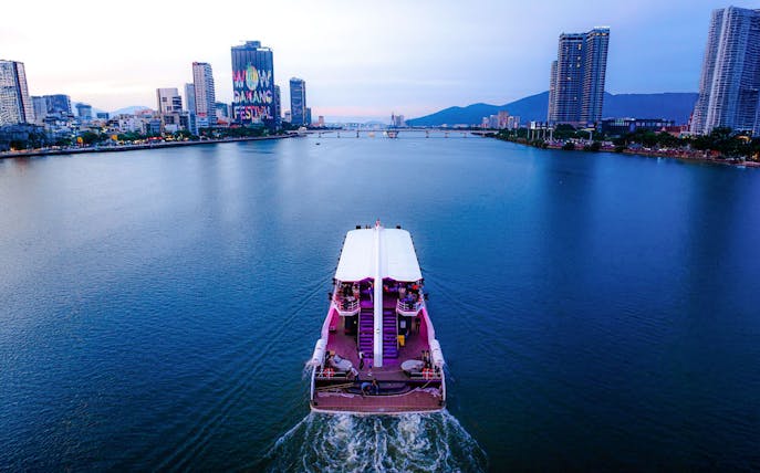 Cruise ship on Han River with Da Nang skyline and festival sign in view.