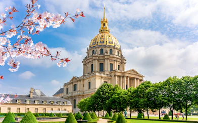 Les Invalides Dome in Paris with cherry blossoms and manicured gardens.