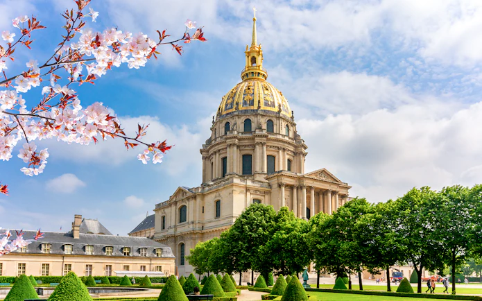 Les Invalides Dome in Paris with cherry blossoms and manicured gardens.