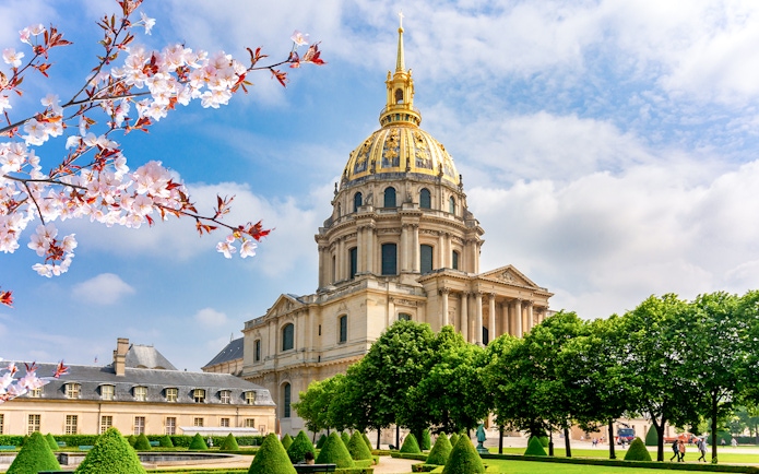 Les Invalides Dome in Paris with cherry blossoms and manicured gardens.