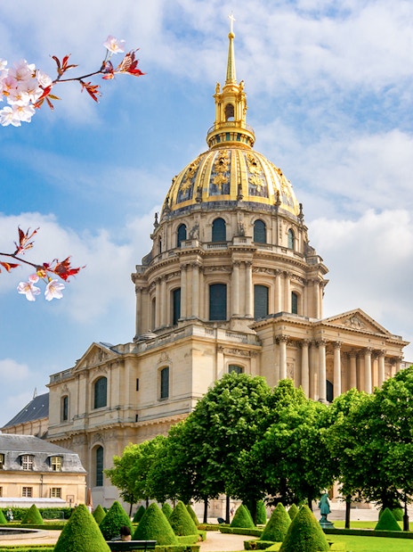 Les Invalides Dome in Paris with cherry blossoms and manicured gardens.