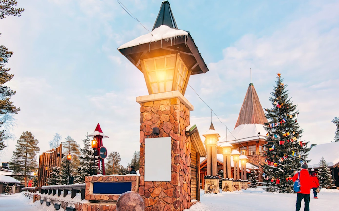 Santa Claus Village entrance with Christmas tree and visitors in Rovaniemi.