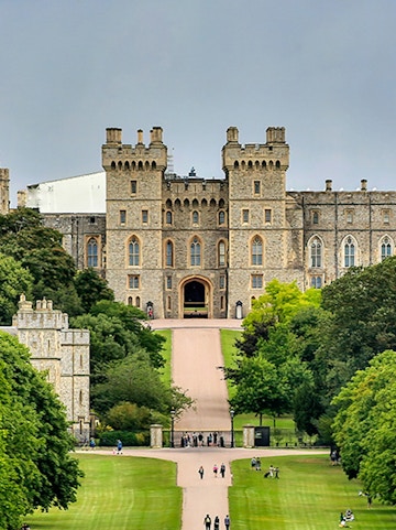 Windsor Castle entrance with visitors on the path, surrounded by lush greenery.