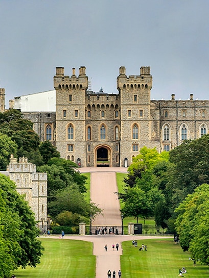 Windsor Castle entrance with visitors on the path, surrounded by lush greenery.
