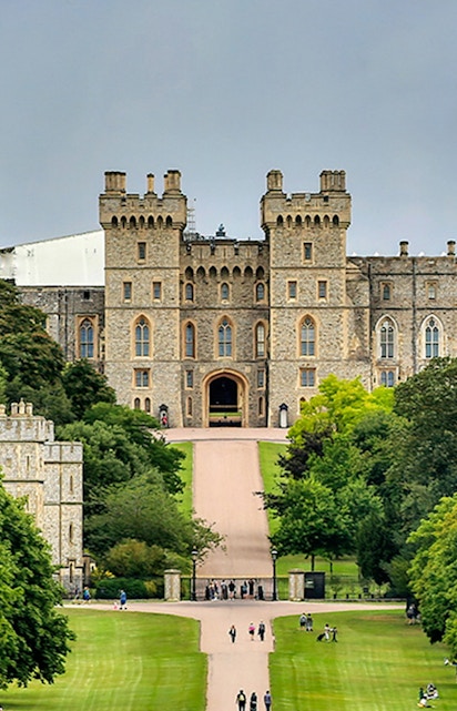 Windsor Castle entrance with visitors on the path, surrounded by lush greenery.