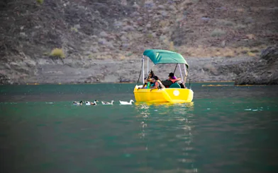 People on a yellow pedal boat in Hatta Lake, surrounded by mountains, Sharjah.