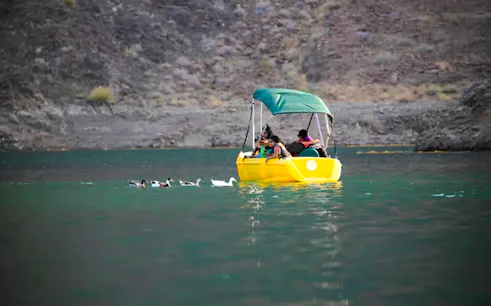 People on a yellow pedal boat in Hatta Lake, surrounded by mountains, Sharjah.