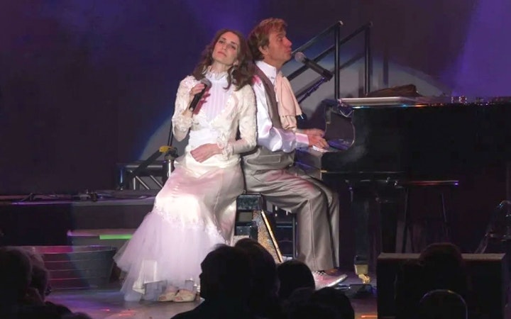 Performers on stage during Carpenters Legacy show, with one singing and the other playing piano.