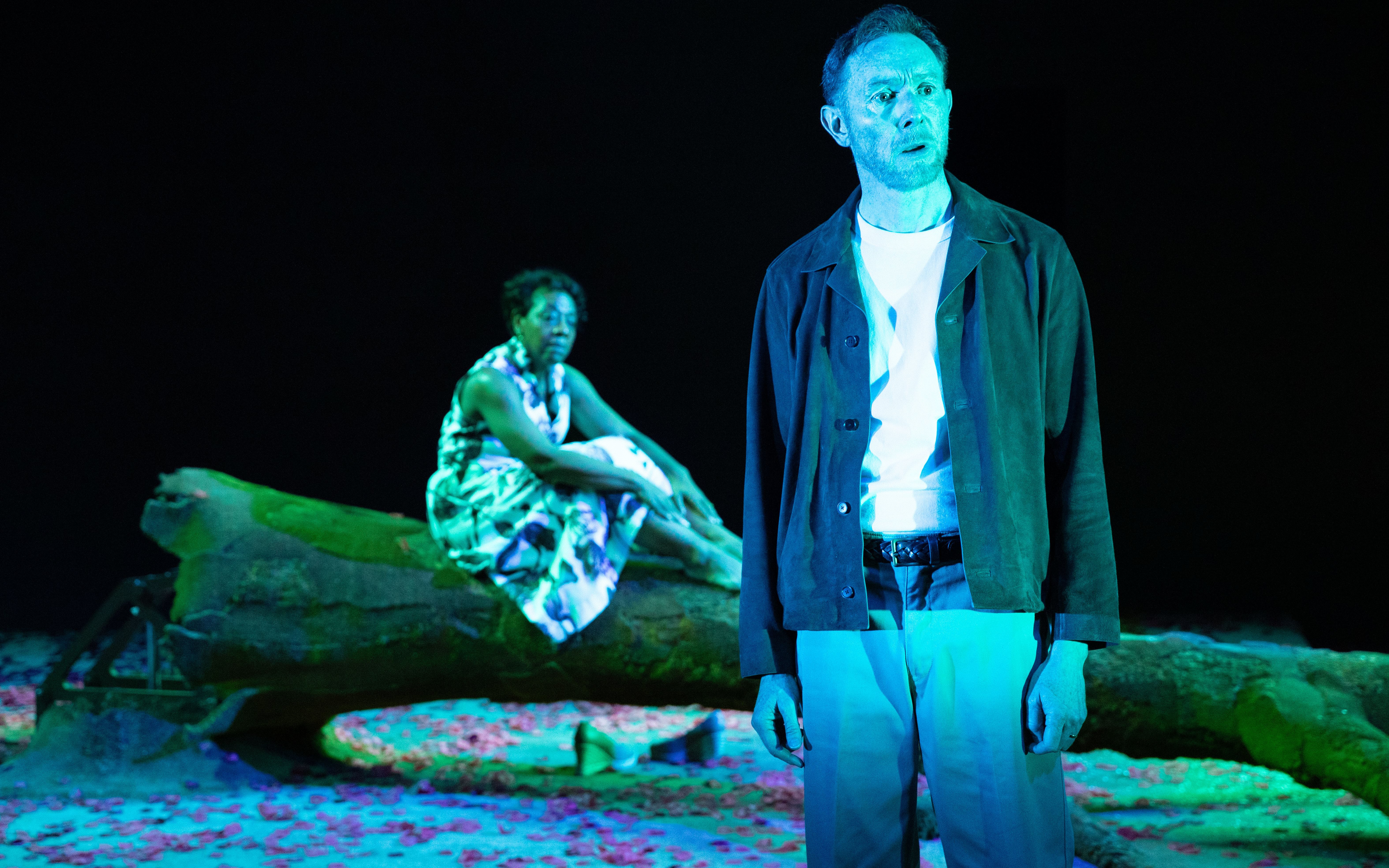 Actors performing in "All My Sons" on a West End stage, with one seated on a log.