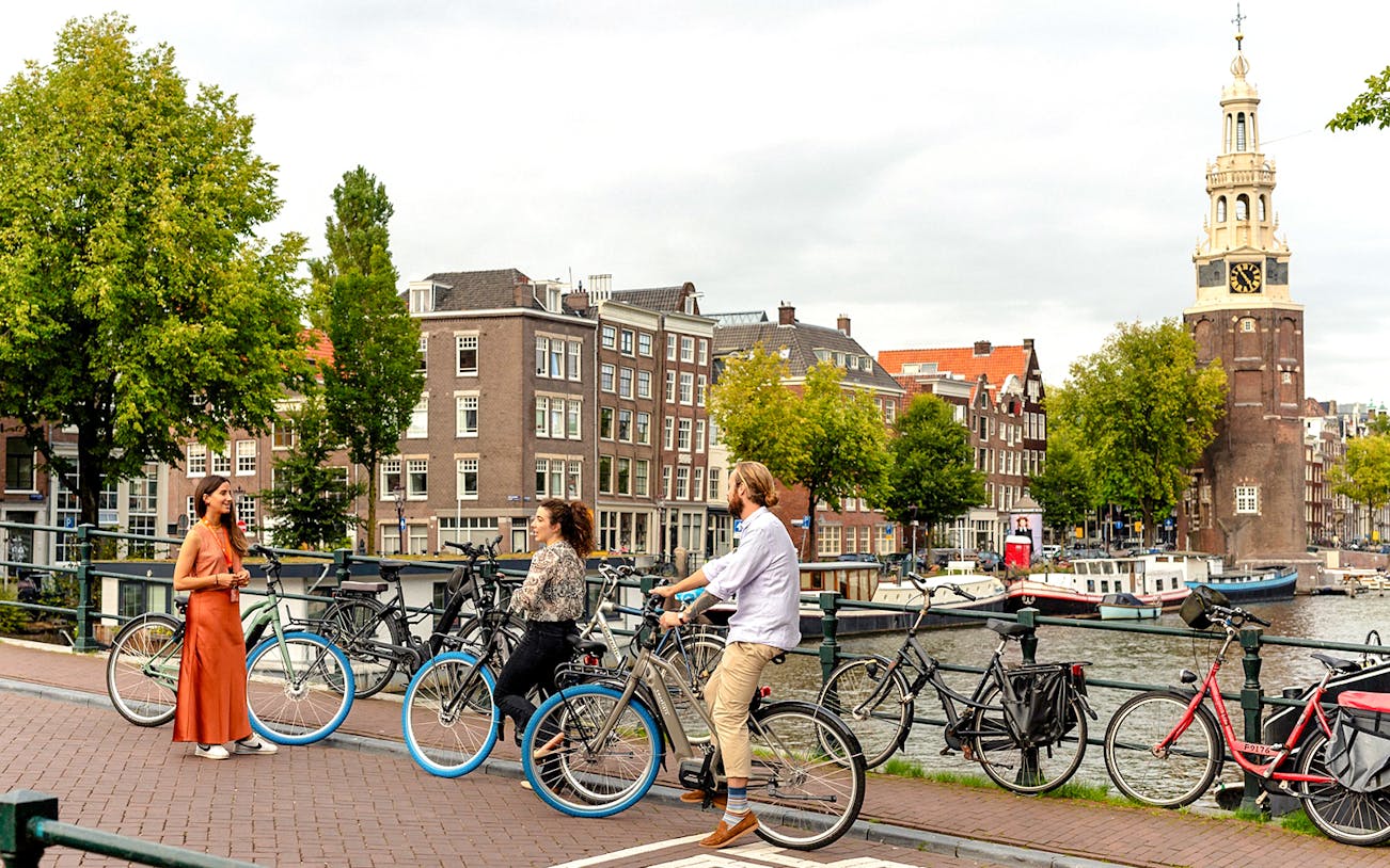 Cyclists on a canal bridge in Amsterdam with Montelbaanstoren tower in view.