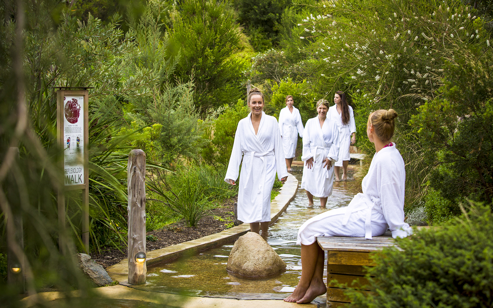 Visitors in white robes walking through a reflexology path at Peninsula Hot Springs.