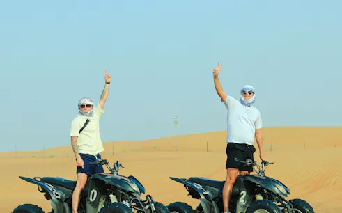 Two people on ATVs in Dubai desert during quad biking tour.