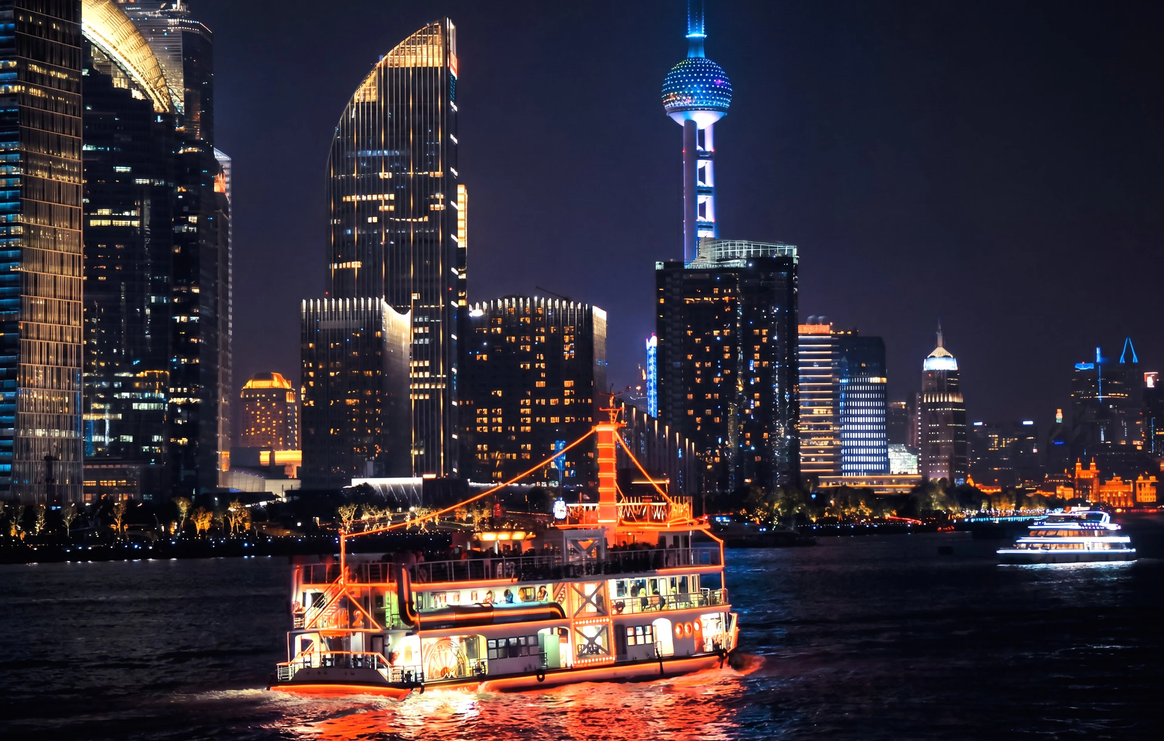 Illuminated cruise on Huangpu River with Shanghai skyline at night.