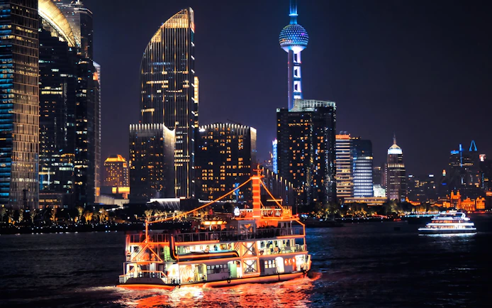Illuminated cruise on Huangpu River with Shanghai skyline at night.
