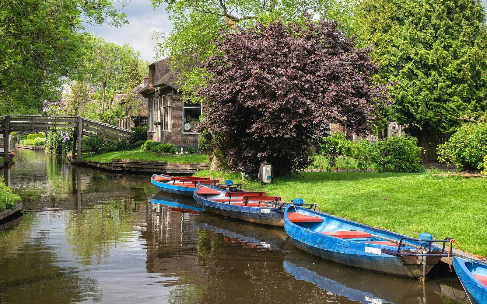Boats on a canal in Giethoorn with a wooden bridge and traditional house.