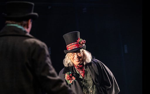 Character in Victorian attire with top hat in "A Sherlock Carol" performance.