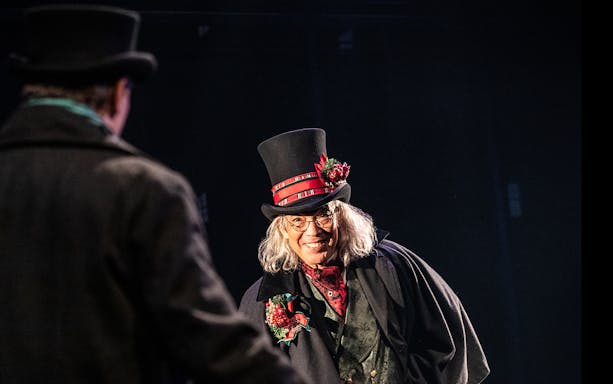 Character in Victorian attire with top hat in "A Sherlock Carol" performance.
