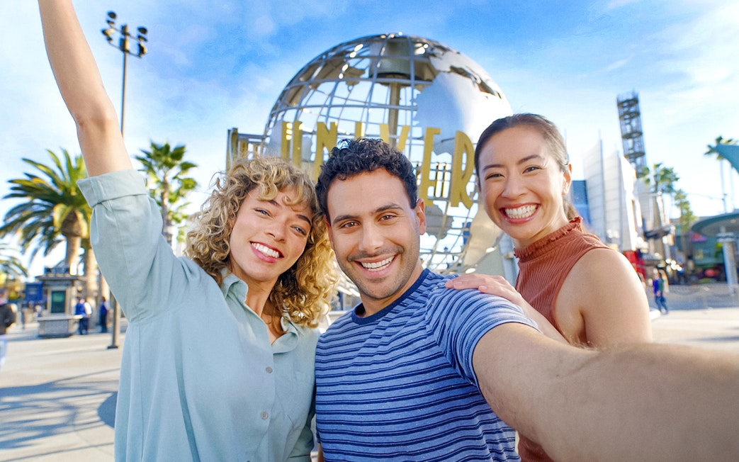 Visitors smiling in front of the Universal Studios Hollywood globe.