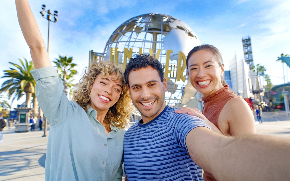 Visitors smiling in front of the Universal Studios Hollywood globe.