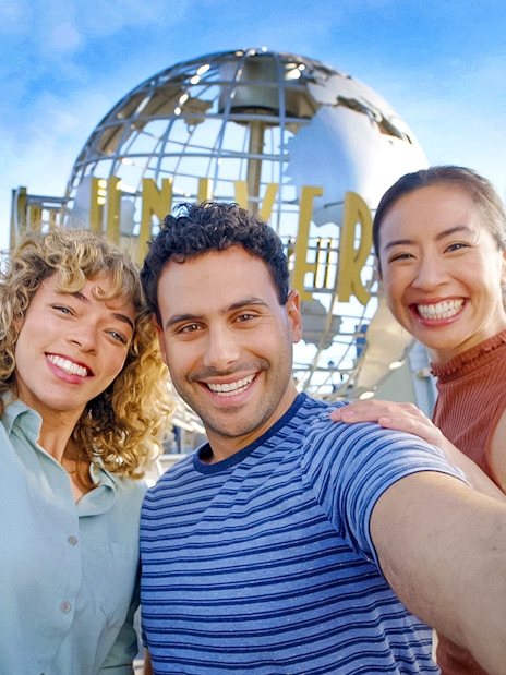Visitors smiling in front of the Universal Studios Hollywood globe.