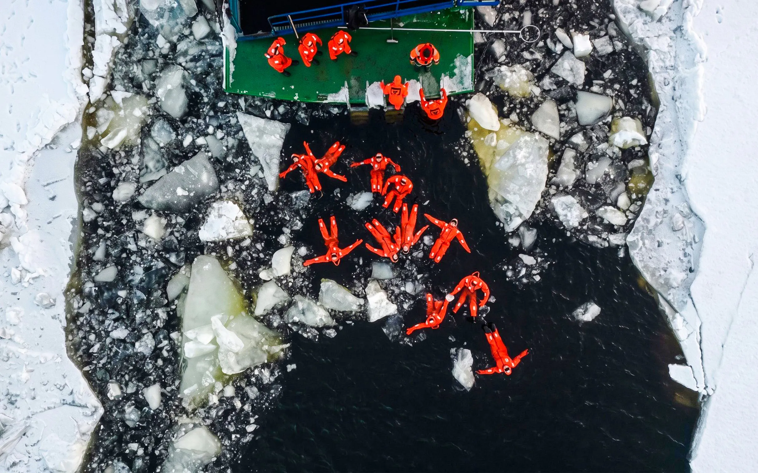 Guests in orange suits floating among ice during Icebreaker Cruise & Ice Floating Experience.