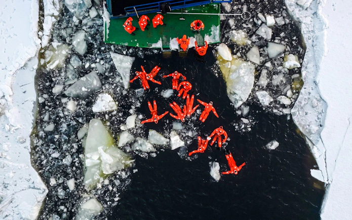 Guests in orange suits floating among ice during Icebreaker Cruise & Ice Floating Experience.