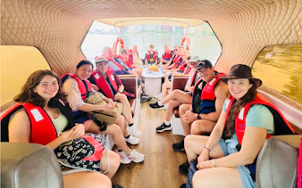 Group on speed boat for VIP Cu Chi Tunnels tour, wearing life jackets, river view in background.