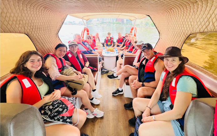 Group on speed boat for VIP Cu Chi Tunnels tour, wearing life jackets, river view in background.