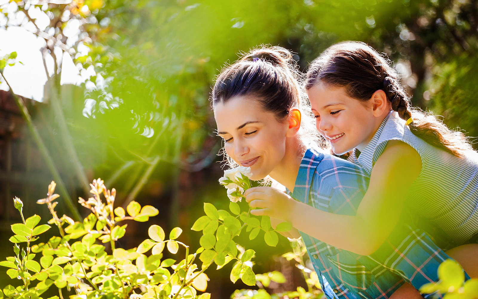 Mother and daughter enjoying flowers in a sunlit garden.