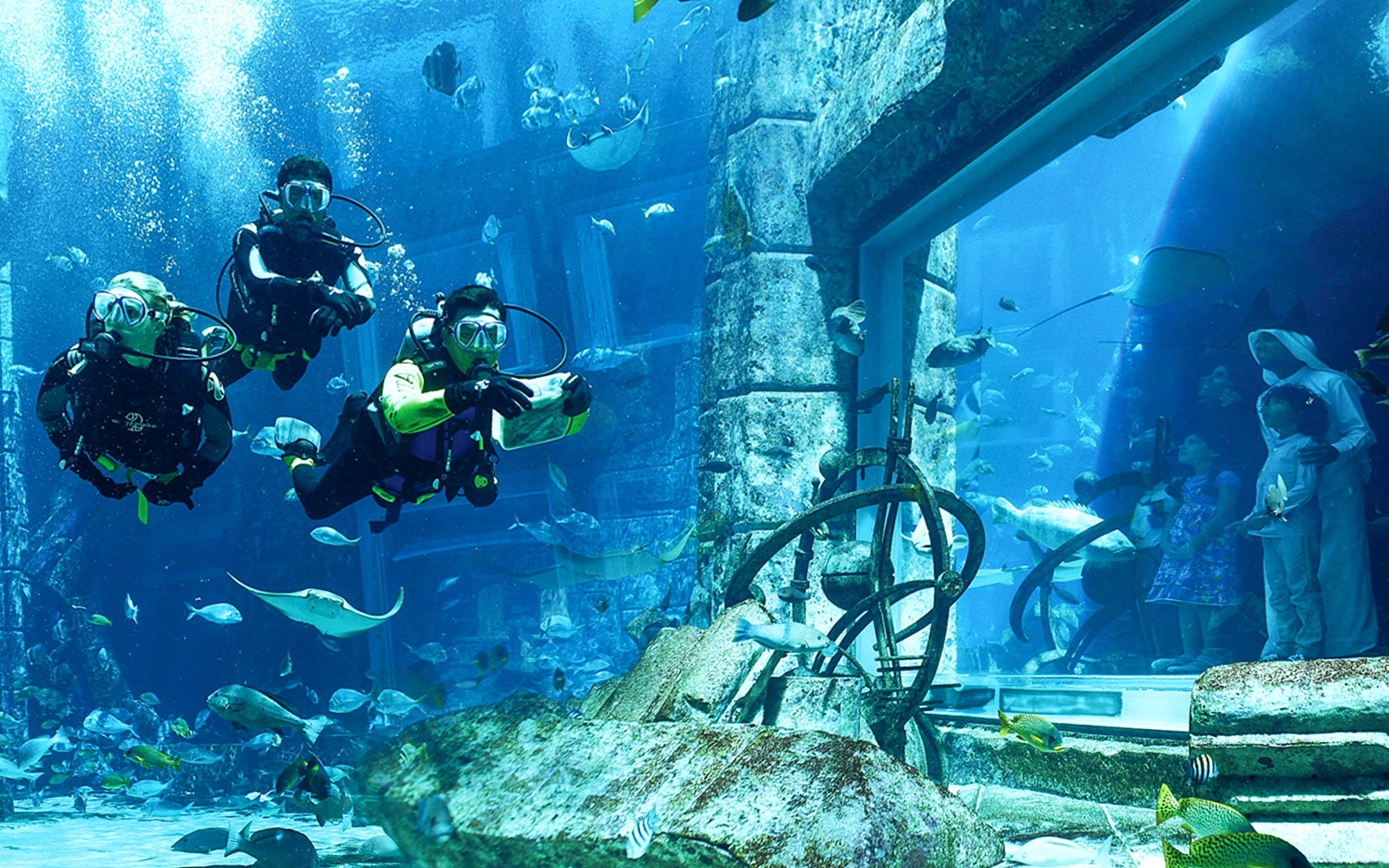 Scuba divers exploring underwater ruins at Atlantis with marine life.