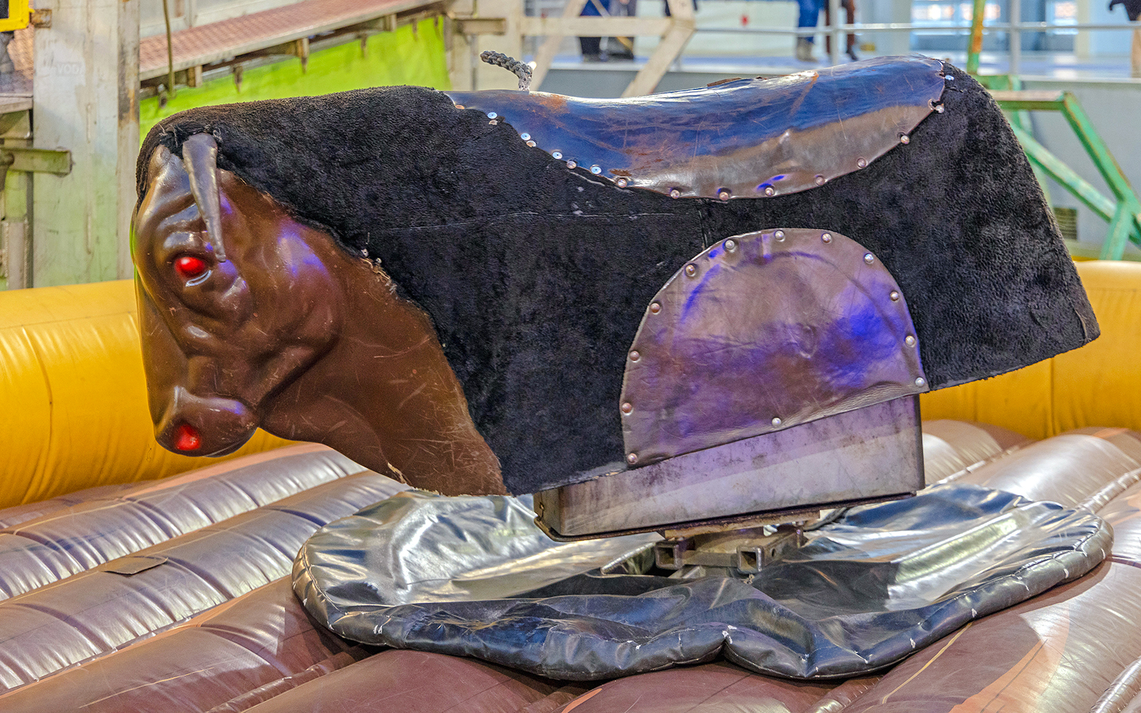 Mechanical bull riding machine with padded base in an indoor setting.