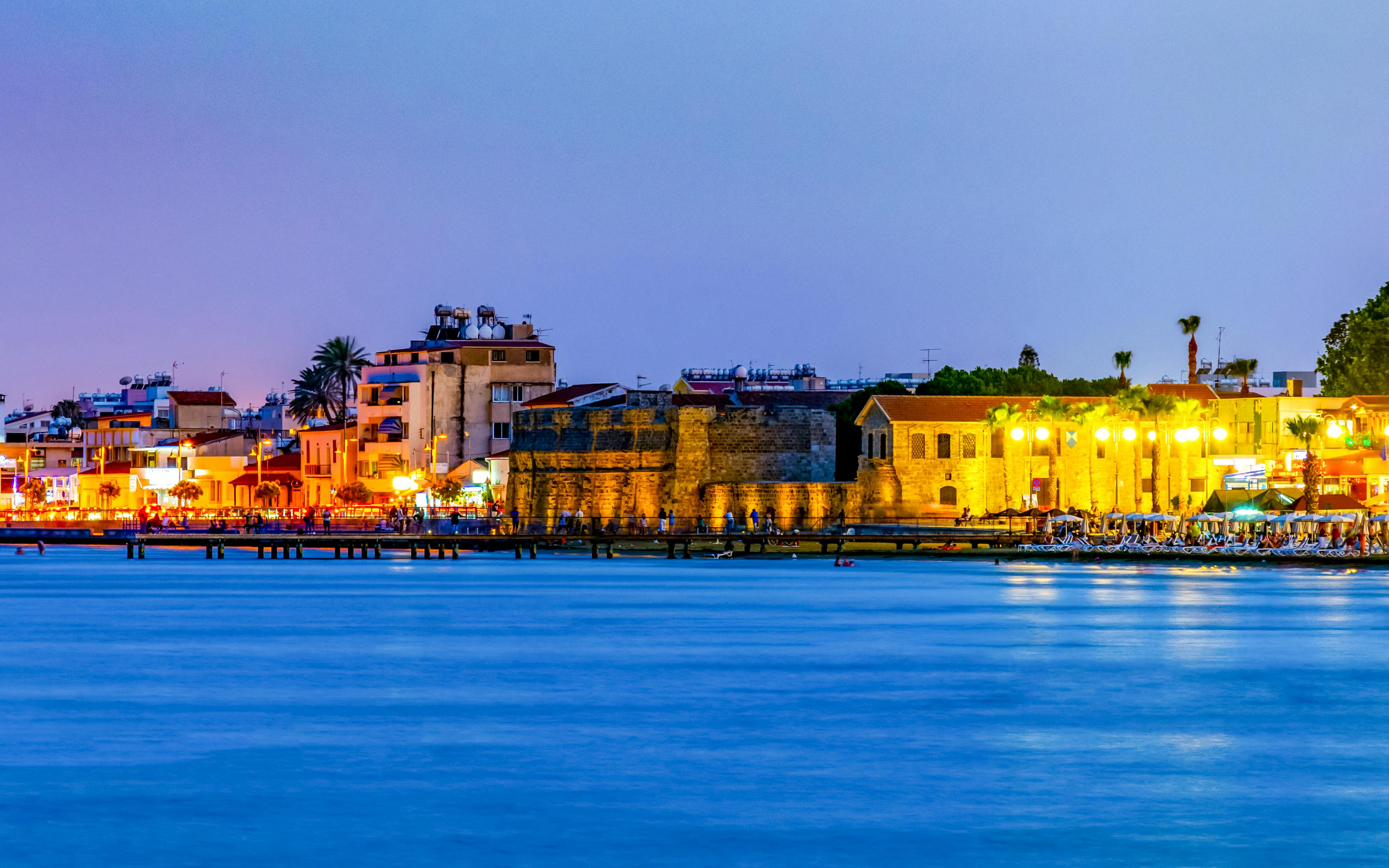 Larnaca waterfront at sunset with historic buildings and vibrant lights.