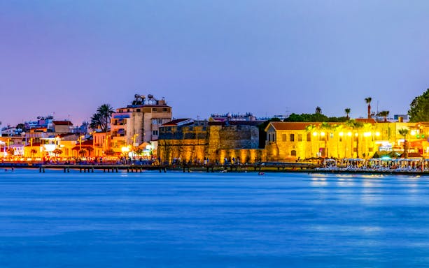 Larnaca waterfront at sunset with historic buildings and vibrant lights.