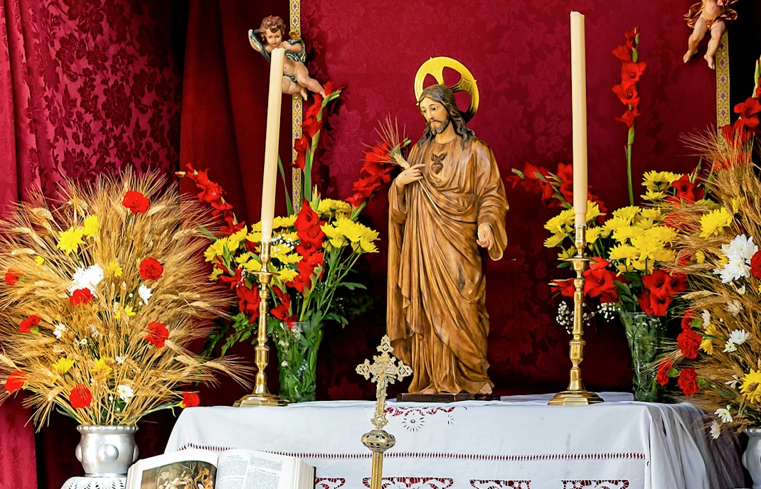Statue of Jesus with flowers and candles during Corpus Christi festival in Spain.