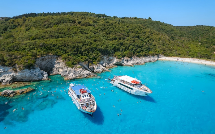 Boats anchored near Paxos and Antipaxos islands with clear blue waters and lush green hills.