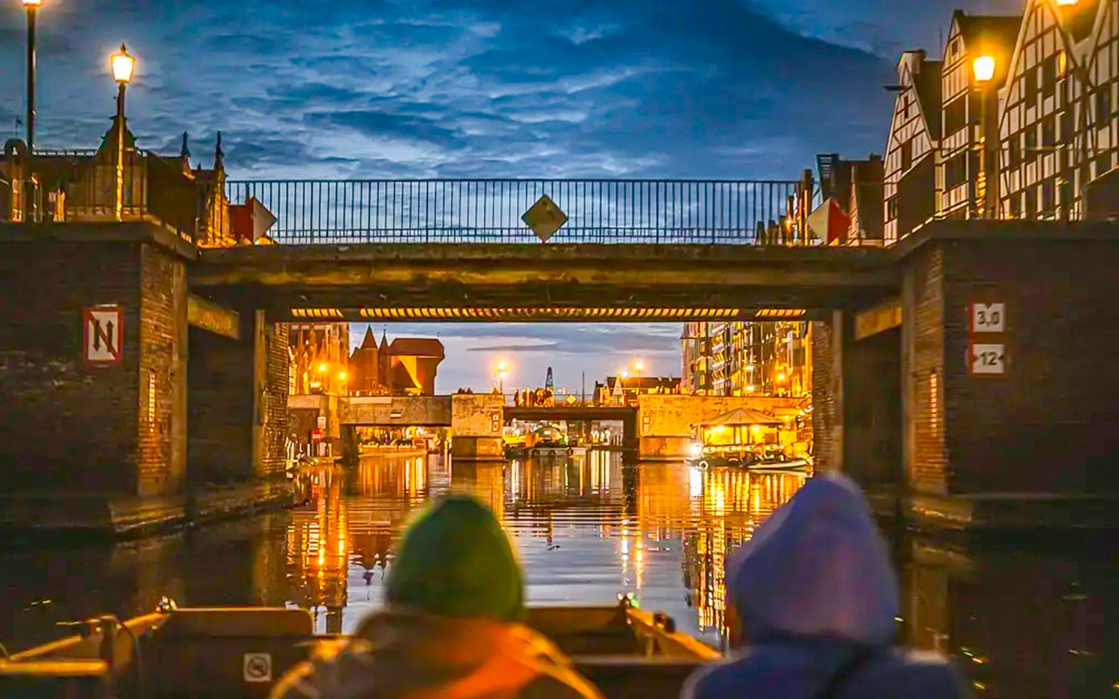 Guests on a historical boat cruise under a bridge in Gdansk at sunset.