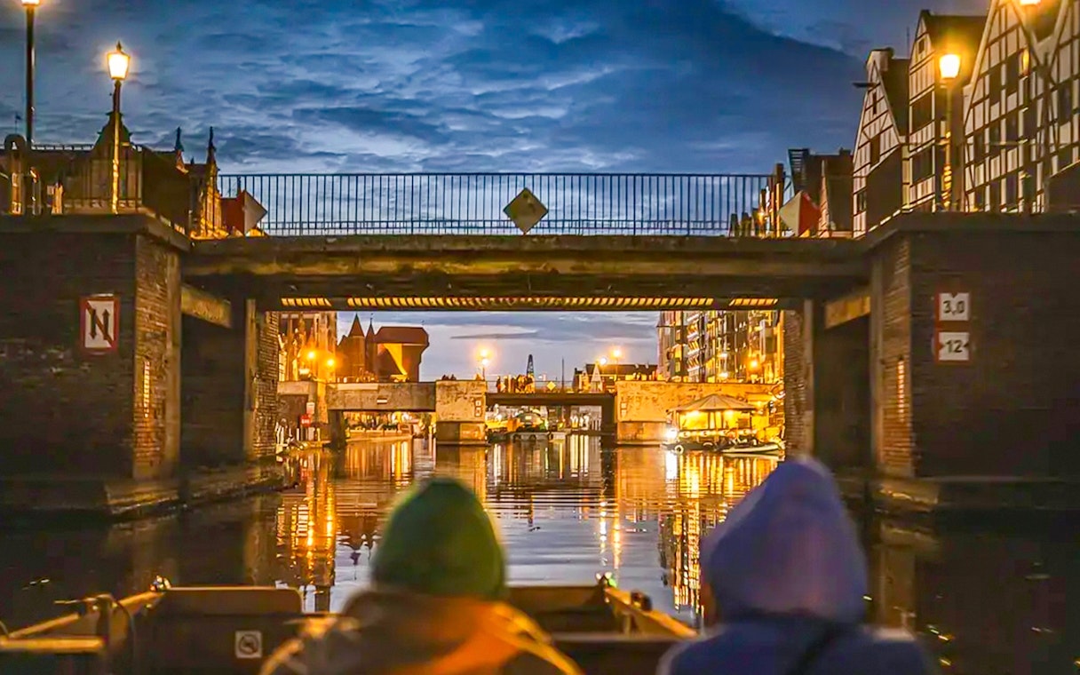 Guests on a historical boat cruise under a bridge in Gdansk at sunset.