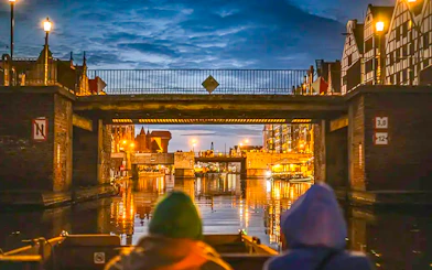 Guests on a historical boat cruise under a bridge in Gdansk at sunset.